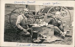 Two men eating a picnic on the grass near a horse-drawn buggy Postcard