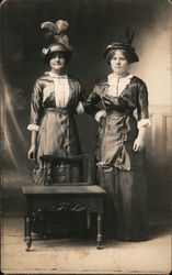 Studio photo of two women holding each others waists, feathered hats Postcard