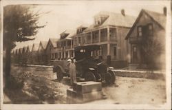 Man in white coveralls posing with truck in middle of residential street Postcard