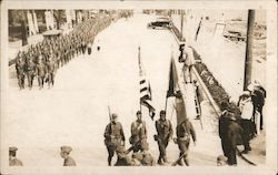 Man on ladder taking picture of marching troops coming down street Postcard