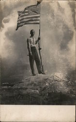 Man with American Flag on makeshift flagpole atop a rock Postcard