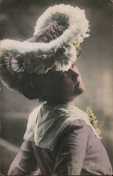 A woman in a purple dress with a wide, white collar in a large flower trimmed hat looks toward the right. Postcard