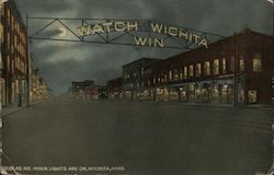 Douglas Ave when light are on, Wichita, Kans. - A street with store lights and a sign that says, "Watch Wichita Win" Kansas Post Postcard