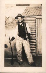 Smiling cowboy in wooly chaps and holding a rifle and rope. Postcard