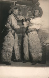 Two Men Dressed as Cowboys Wearing Wooly Chaps - One Holding the Other at Gunpoint Postcard